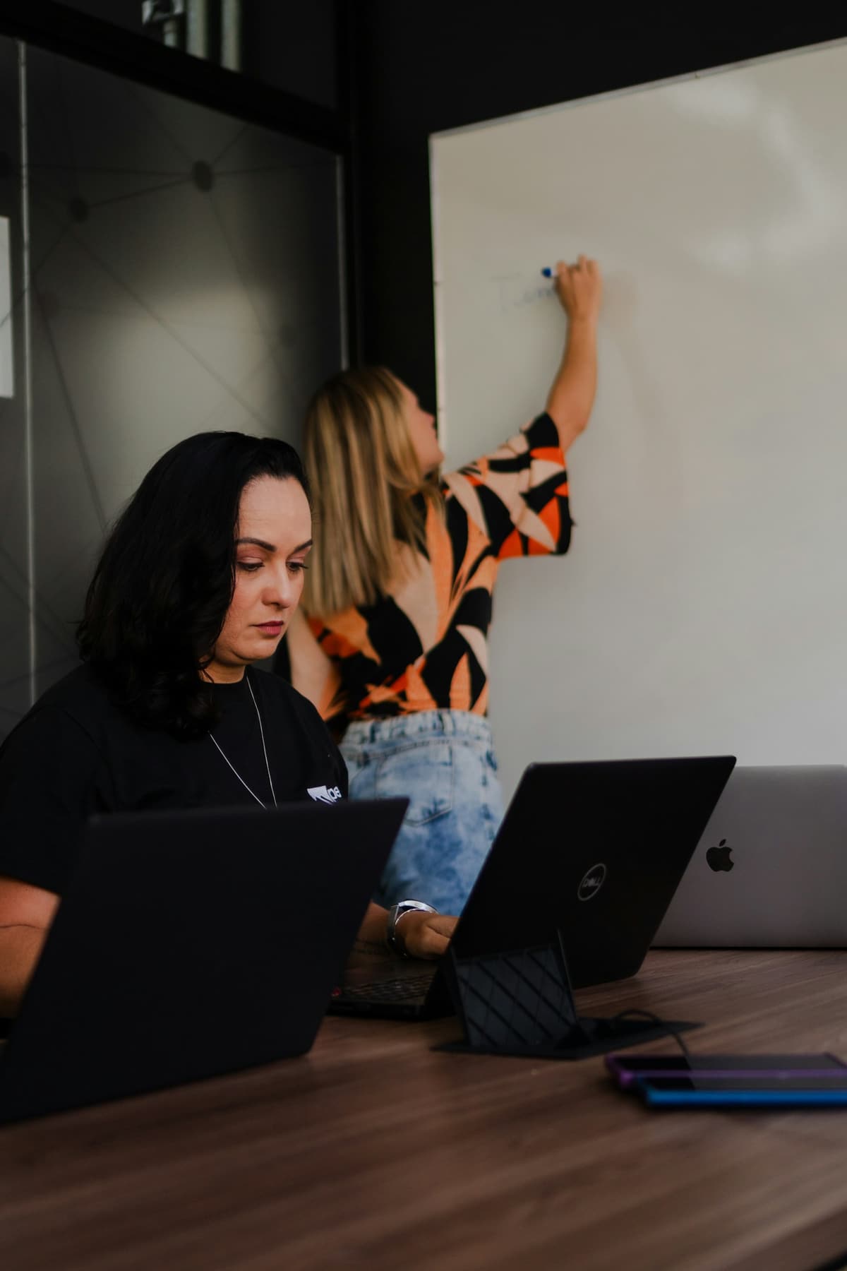 Two engineers working at laptops beside a whiteboard